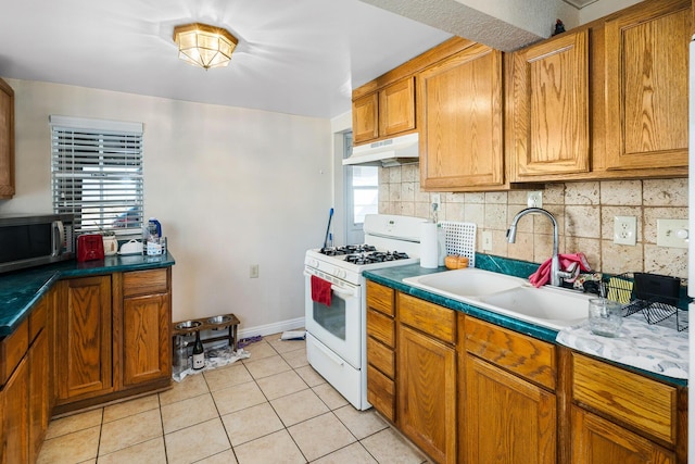 kitchen with light tile patterned flooring, tasteful backsplash, white range with gas cooktop, and sink