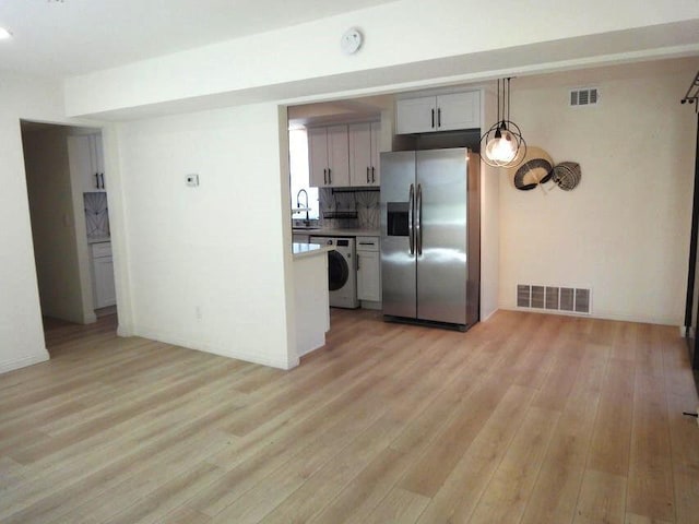 kitchen featuring stainless steel refrigerator with ice dispenser, decorative backsplash, washer / dryer, and light wood-type flooring