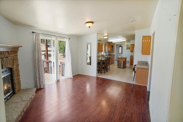 living room with a textured ceiling, light wood-type flooring, and a stone fireplace