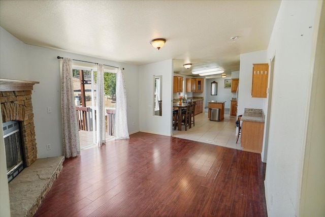 living room with a stone fireplace, light hardwood / wood-style flooring, and a textured ceiling