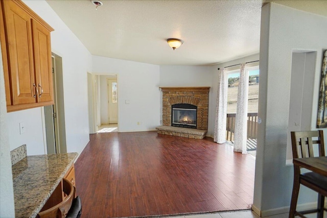 living room with a textured ceiling, dark hardwood / wood-style floors, and a stone fireplace