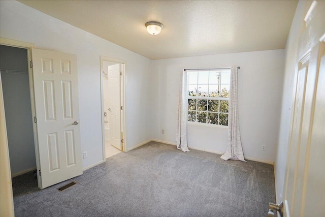 unfurnished bedroom featuring carpet flooring, ensuite bathroom, a closet, and lofted ceiling