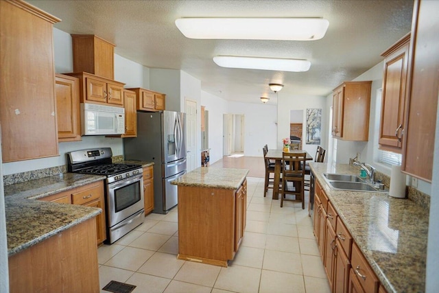 kitchen with appliances with stainless steel finishes, dark stone counters, sink, light tile patterned floors, and a center island