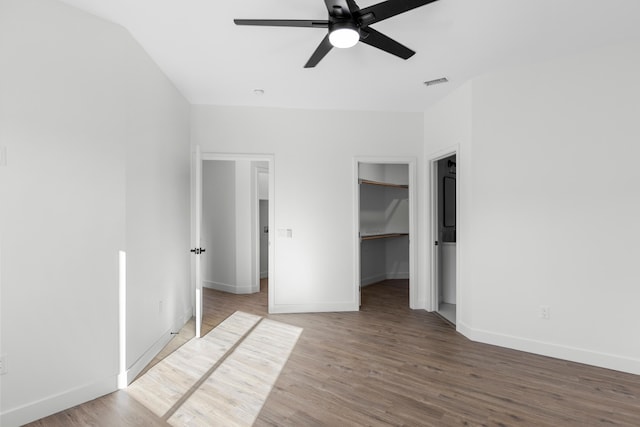 unfurnished bedroom with ceiling fan, a spacious closet, lofted ceiling, and hardwood / wood-style flooring