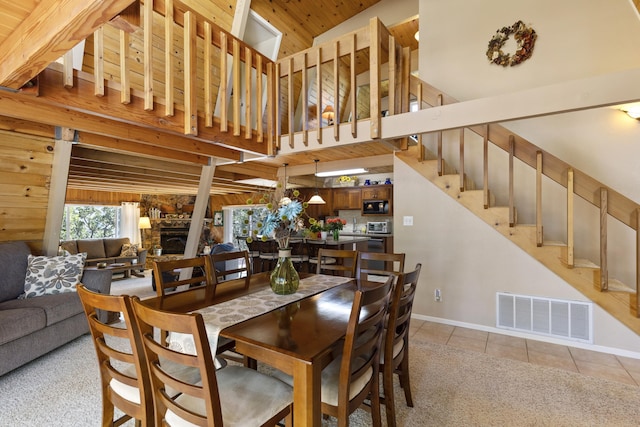 dining room with a high ceiling, light tile patterned flooring, a stone fireplace, and wood walls