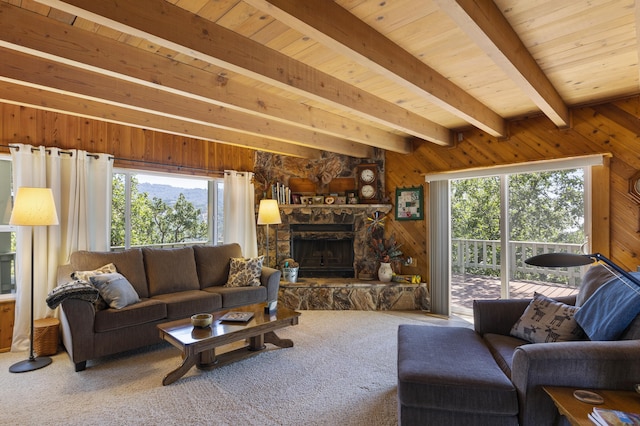 carpeted living room with a healthy amount of sunlight, a stone fireplace, beamed ceiling, and wood walls