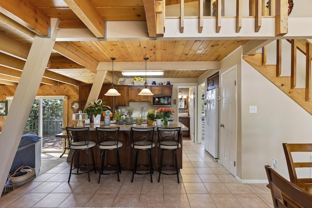 kitchen featuring pendant lighting, black microwave, a breakfast bar area, white refrigerator, and light tile patterned floors