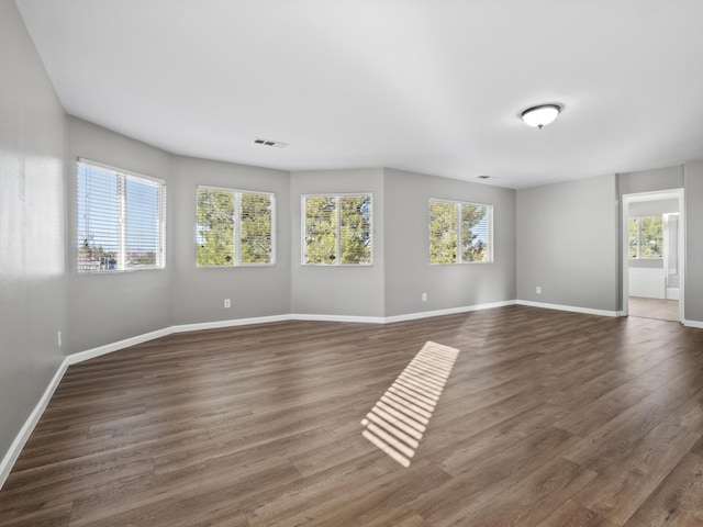 spare room featuring dark wood-type flooring, plenty of natural light, visible vents, and baseboards