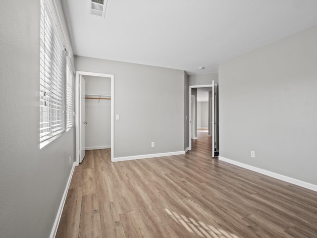 unfurnished bedroom featuring light wood finished floors, a closet, visible vents, a spacious closet, and baseboards