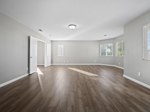 unfurnished room featuring visible vents, dark wood finished floors, and baseboards