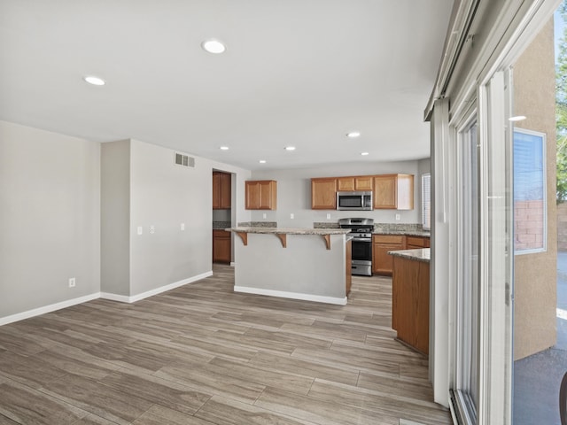 kitchen featuring visible vents, appliances with stainless steel finishes, brown cabinets, a center island, and a kitchen bar