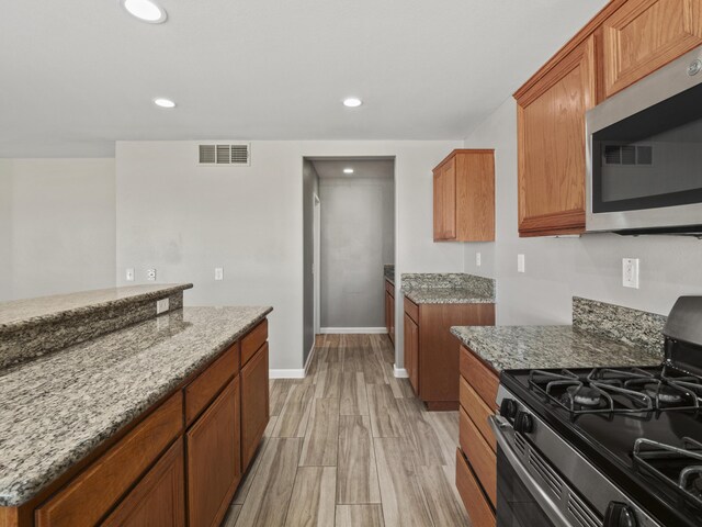 kitchen featuring visible vents, gas range, stainless steel microwave, brown cabinets, and light stone counters