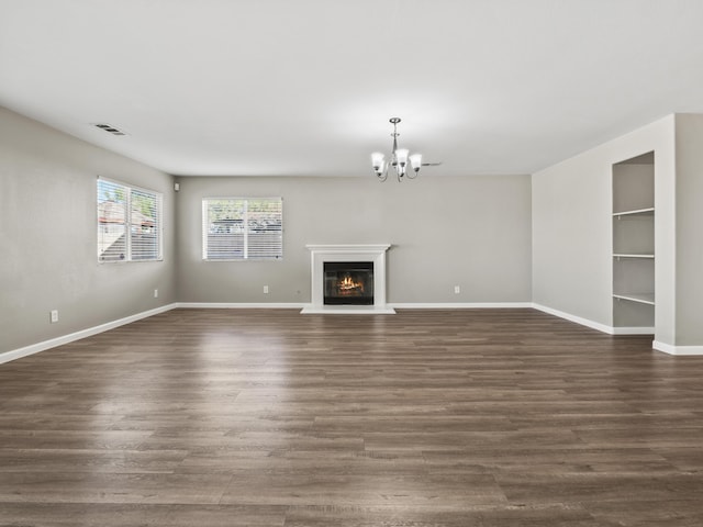 unfurnished living room with a glass covered fireplace, dark wood-style flooring, a notable chandelier, and baseboards