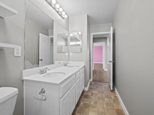 bathroom with stone finish floor, a sink, baseboards, and double vanity