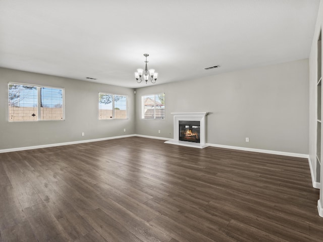 unfurnished living room featuring visible vents, baseboards, dark wood-style floors, a glass covered fireplace, and an inviting chandelier