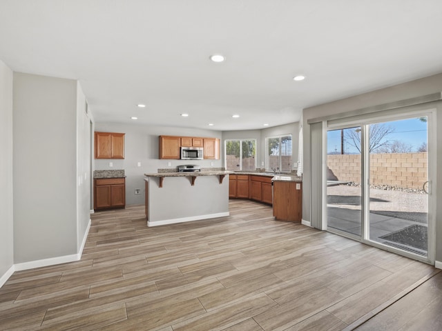 kitchen with brown cabinetry, a kitchen island, appliances with stainless steel finishes, a breakfast bar, and wood tiled floor