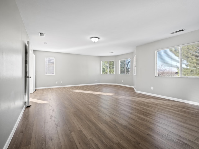 empty room with dark wood-style flooring, visible vents, and baseboards