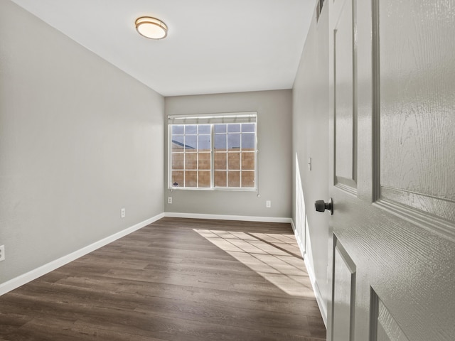 empty room featuring dark wood-style flooring, visible vents, and baseboards