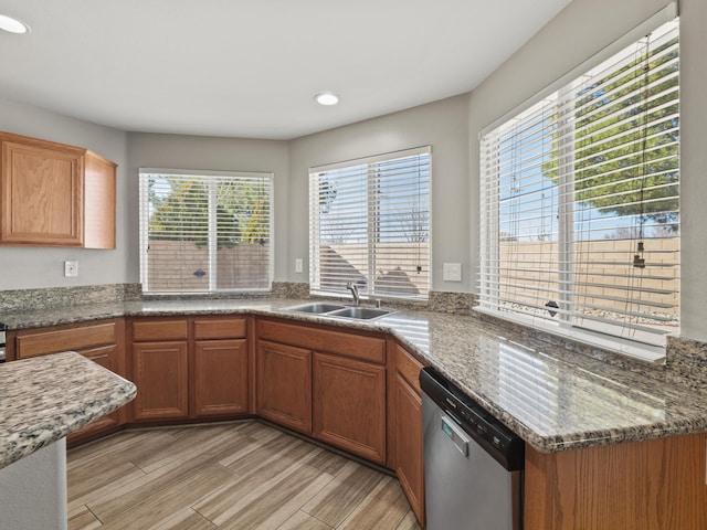 kitchen featuring brown cabinets, dark stone countertops, stainless steel dishwasher, light wood-style floors, and a sink