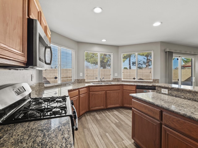 kitchen with brown cabinets, light wood finished floors, stainless steel appliances, a sink, and dark stone counters