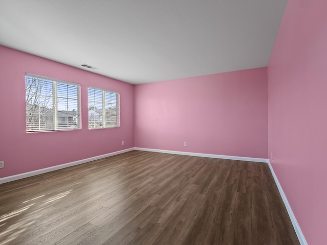 spare room with baseboards, visible vents, and wood finished floors