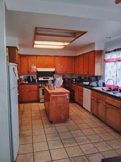 kitchen featuring white appliances, brown cabinets, a center island, under cabinet range hood, and a sink