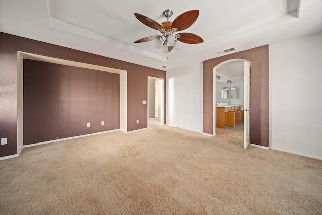 unfurnished bedroom featuring arched walkways, a tray ceiling, light carpet, and visible vents