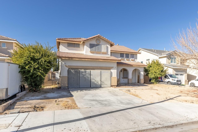 mediterranean / spanish-style home with an attached garage, fence, concrete driveway, a tiled roof, and stucco siding