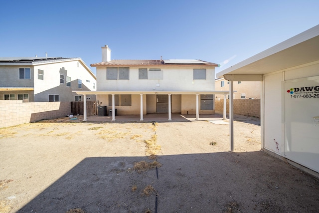 back of house featuring a chimney, solar panels, central AC unit, a patio area, and a fenced backyard