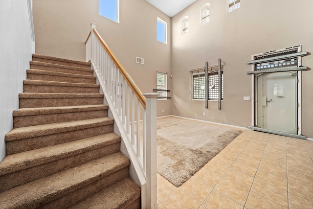 stairway with a healthy amount of sunlight, a high ceiling, visible vents, and tile patterned floors