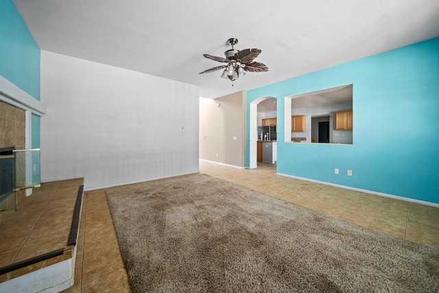 unfurnished living room with tile patterned flooring, a fireplace, arched walkways, and a ceiling fan