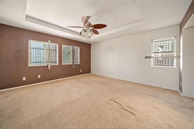 carpeted spare room with a ceiling fan and a tray ceiling