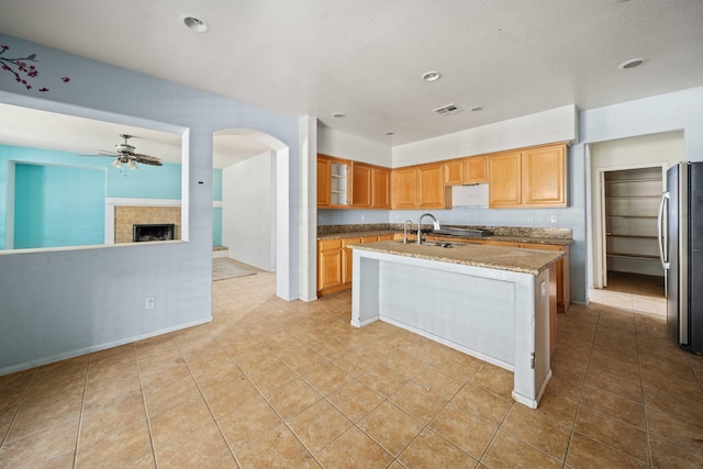 kitchen featuring a kitchen island with sink, a sink, freestanding refrigerator, light stone countertops, and glass insert cabinets