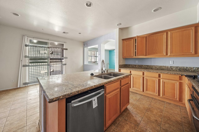 kitchen with visible vents, brown cabinets, a kitchen island with sink, stainless steel dishwasher, and a sink