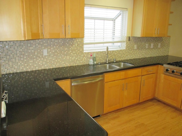 kitchen with stainless steel appliances, dark stone countertops, backsplash, a sink, and light wood-style flooring