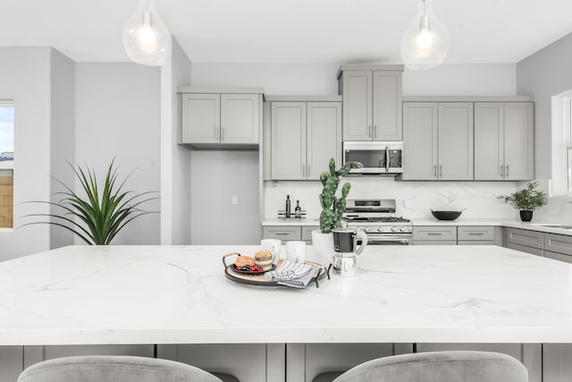 kitchen featuring a center island, a kitchen breakfast bar, pendant lighting, gray cabinets, and appliances with stainless steel finishes