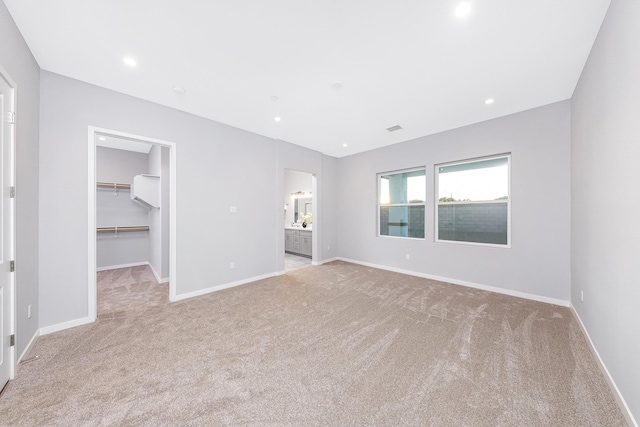 unfurnished bedroom featuring ensuite bathroom, light colored carpet, a spacious closet, and a closet