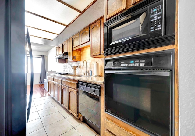 kitchen featuring black appliances, decorative backsplash, sink, light tile patterned flooring, and light stone counters