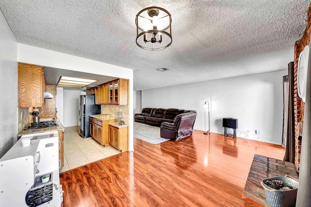 kitchen featuring decorative backsplash, black fridge, stainless steel gas cooktop, a chandelier, and light hardwood / wood-style flooring