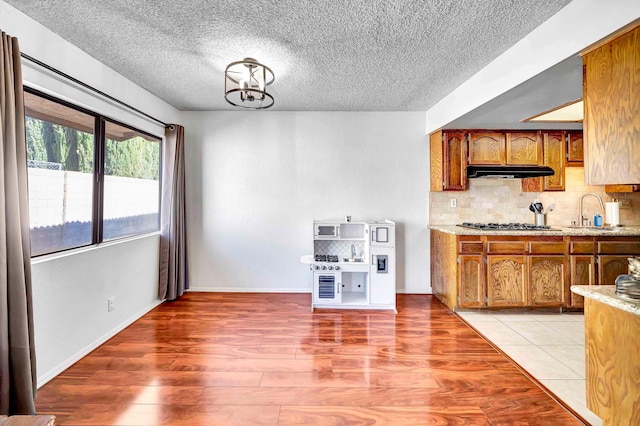 kitchen featuring sink, backsplash, stainless steel gas stovetop, a notable chandelier, and light hardwood / wood-style flooring