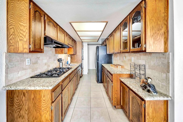 kitchen with backsplash, stainless steel gas stovetop, black fridge, sink, and light tile patterned floors