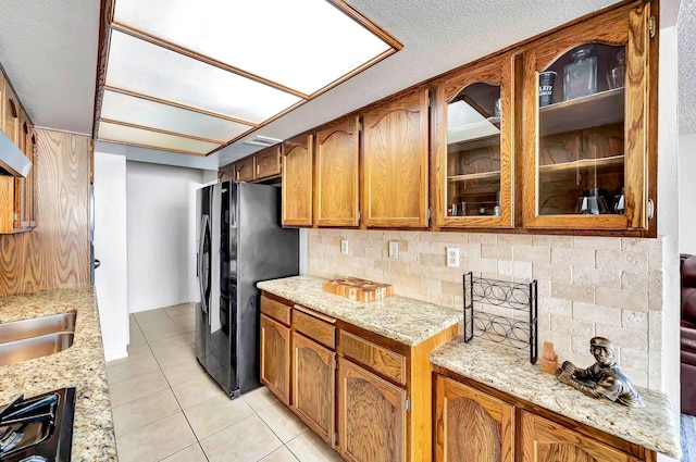 kitchen with light stone counters, decorative backsplash, light tile patterned floors, and black fridge