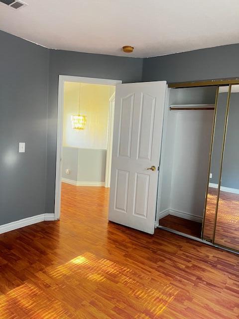 unfurnished bedroom featuring an inviting chandelier, wood-type flooring, and a closet