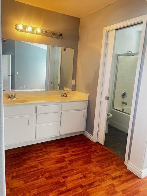 full bathroom with shower / bath combination with glass door, vanity, hardwood / wood-style flooring, and toilet