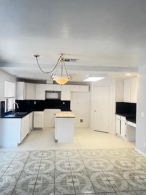 kitchen with white cabinets, a center island, decorative light fixtures, and sink