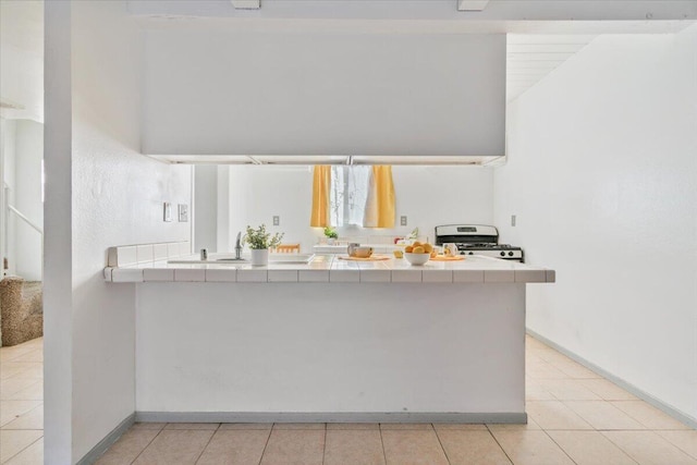 kitchen with tile countertops, stainless steel gas range, light tile patterned flooring, and baseboards