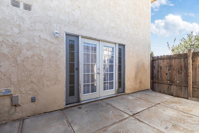 doorway to property featuring french doors, a patio area, fence, and stucco siding