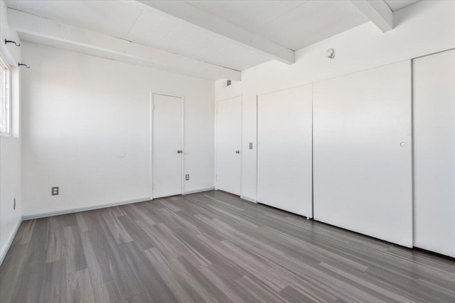 interior space featuring a closet, beamed ceiling, wood finished floors, and baseboards