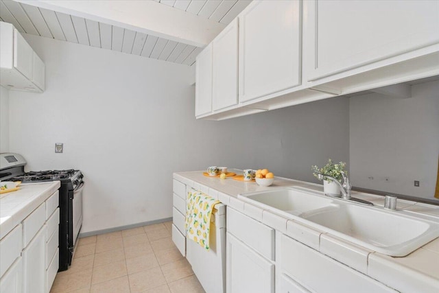 kitchen featuring a sink, stainless steel range with gas cooktop, tile counters, and white cabinetry