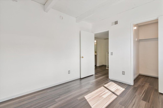 unfurnished bedroom featuring baseboards, visible vents, beam ceiling, and wood finished floors